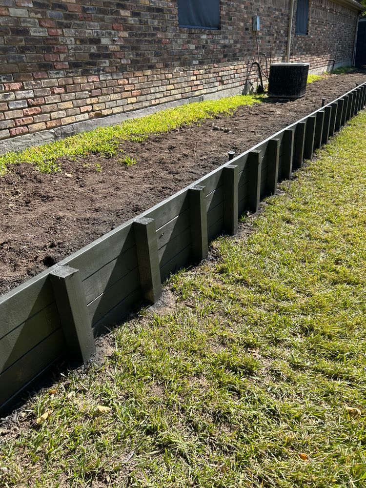 Raised garden bed edging beside a brick wall, with soil and grass in the foreground