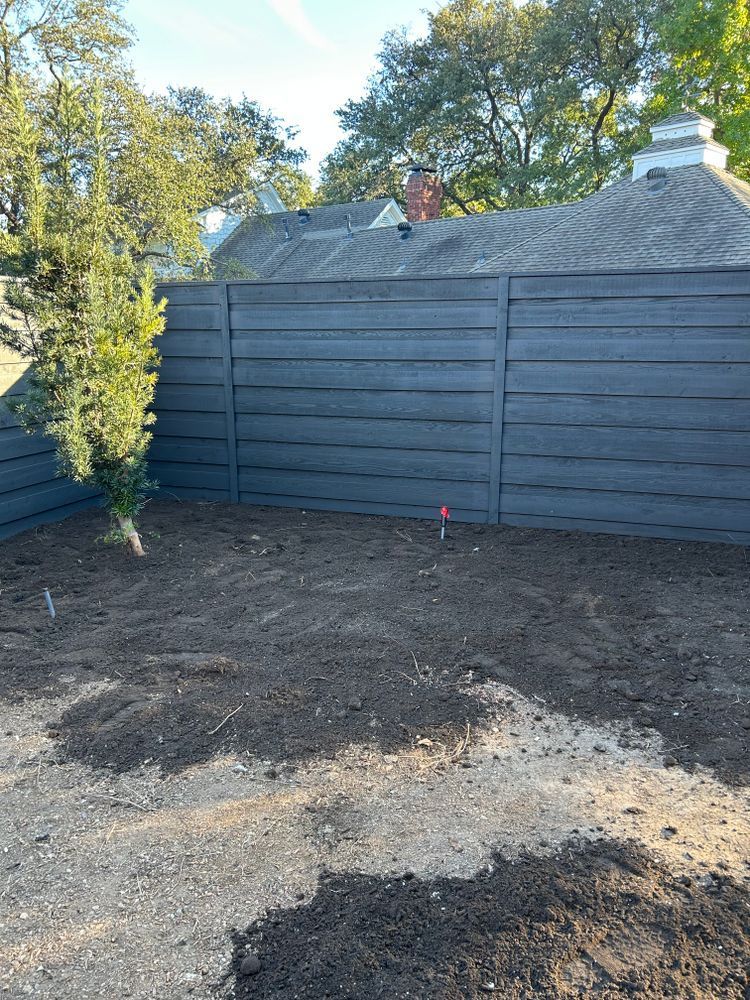 Freshly graded backyard with dark wooden fence and trees in the background