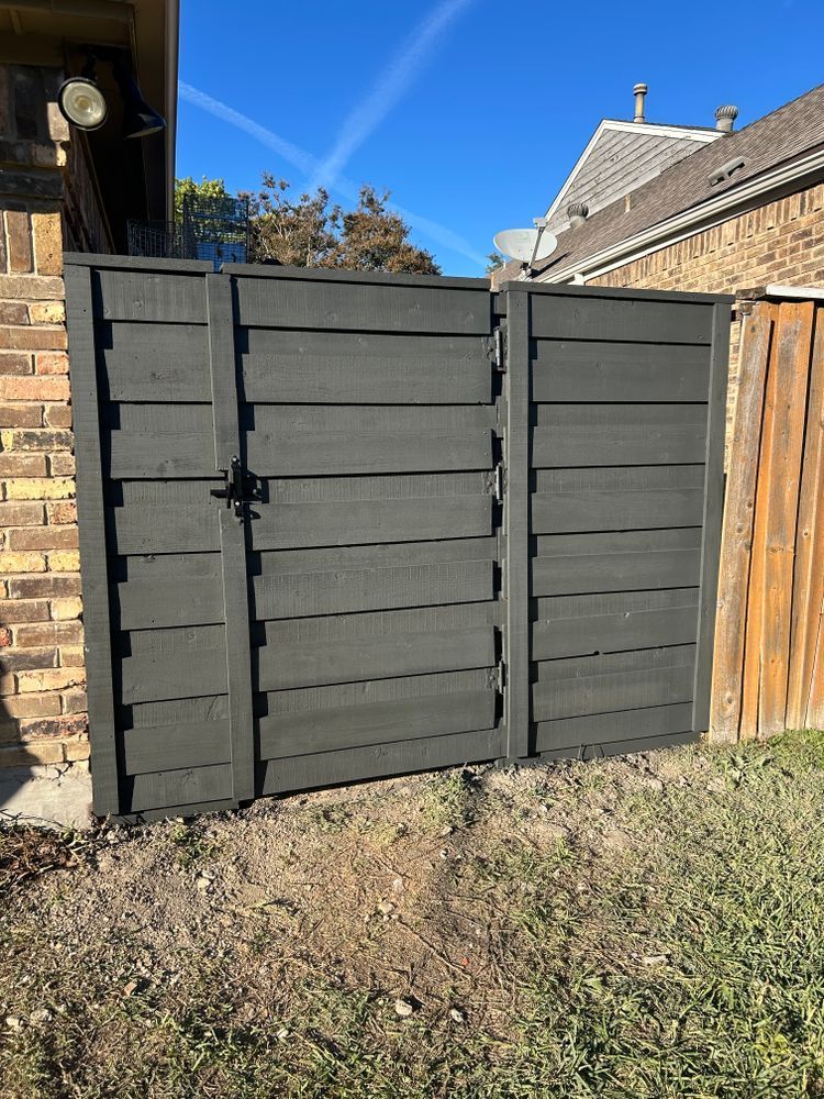 Dark gray wooden garden gate and fence beside a brick wall and wooden fence on a sunny day