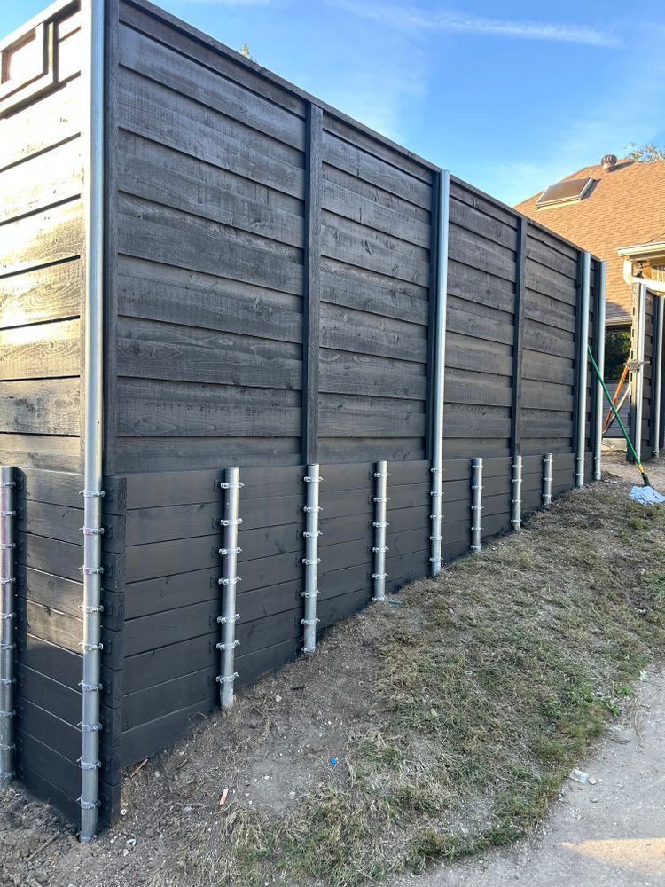 Dark wooden fence with gray posts along a narrow grassy path beside houses