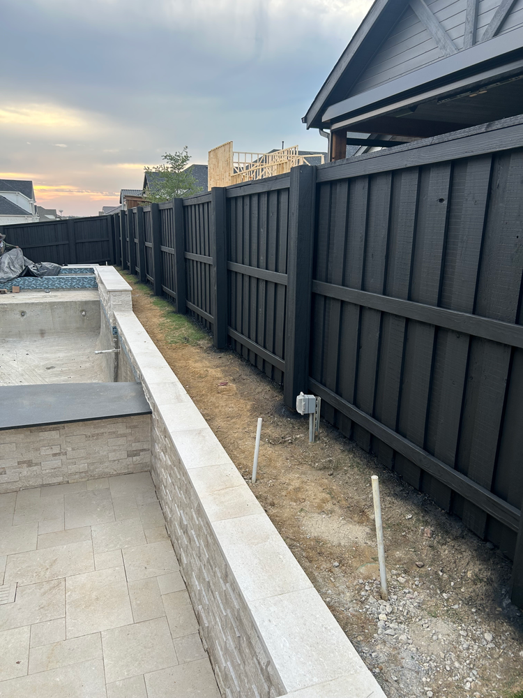 Backyard patio with black privacy fence, gravel strip, and concrete steps beside a house