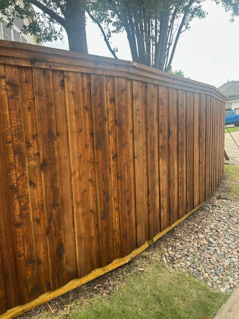 Tall wooden privacy fence beside a gravel strip and grass, with trees behind it.