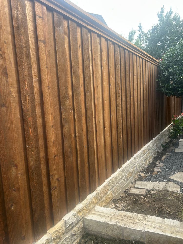 Wooden fence along a narrow gravel path beside a house, with stone edging and trees beyond