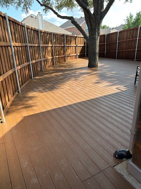 Empty wooden backyard deck with a tree in the center and tall fencing around it