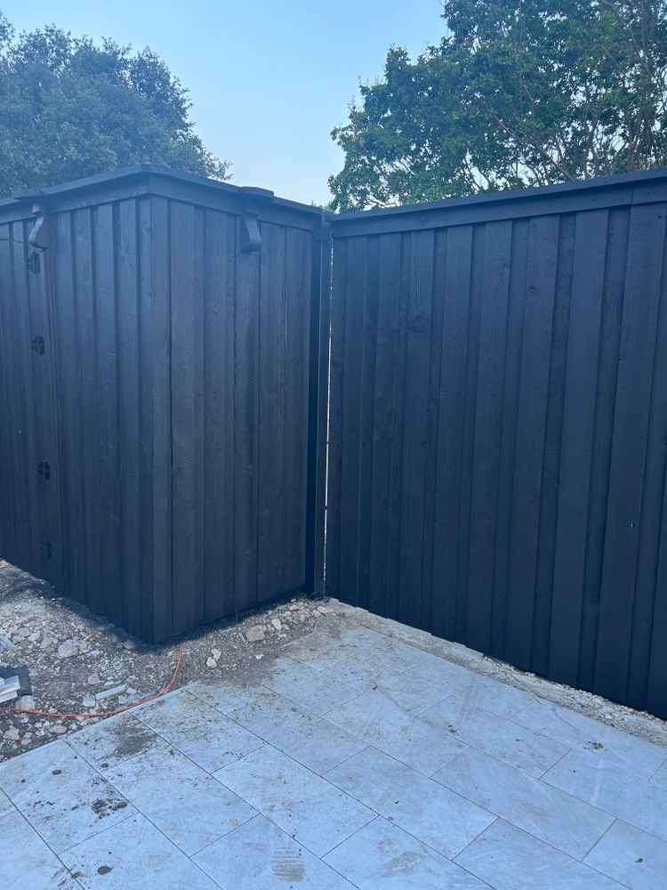 Black wooden fence corner beside a tiled patio under a blue sky