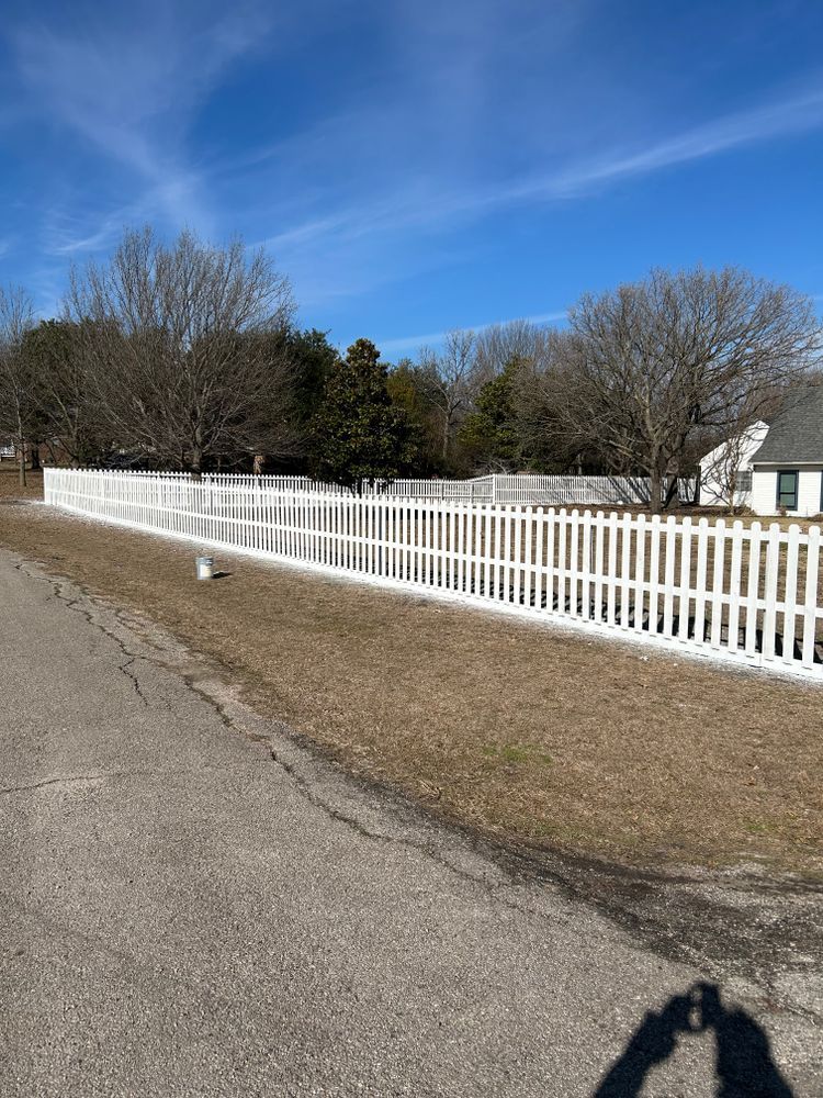 White picket fence along a rural road beside leafless trees under a blue sky