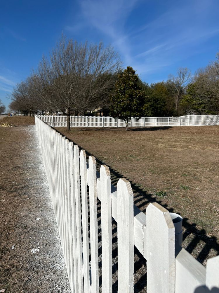White picket fence along a gravel path beside a grassy field under a blue sky