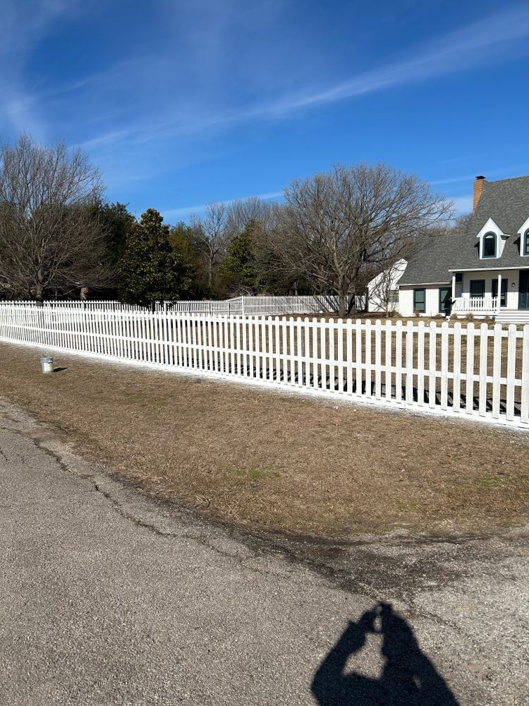White picket fence along a roadside beside a house under a blue sky on a sunny day