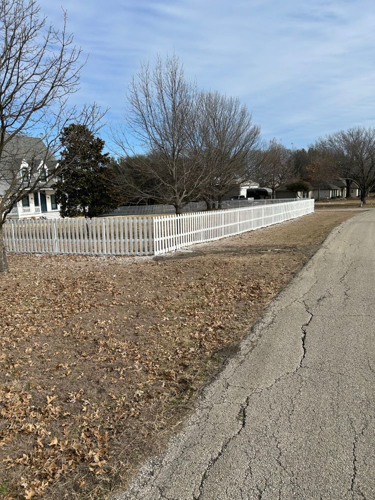 White picket fence along a leaf-covered yard beside a cracked road on a sunny day
