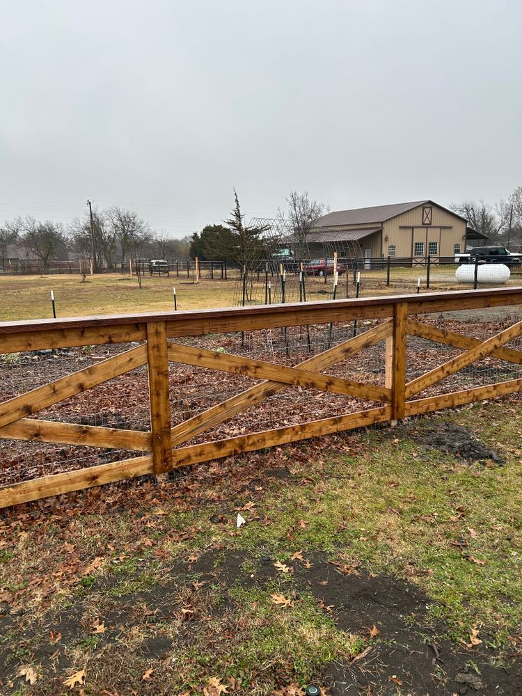 Wooden ranch gate with crisscross fence in a muddy yard, with a house and propane tank in the background
