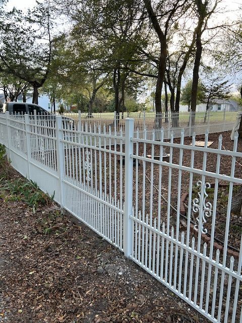 White metal fence along a wooded park path with trees and a house in the background