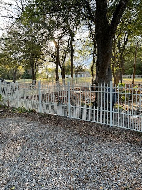 White metal fence around a wooded garden with trees and gravel ground