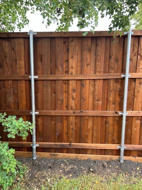 Wooden privacy fence with metal supports in a backyard, with tree branches and shrubs around it