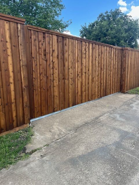 Wooden privacy fence along a concrete driveway with trees in the background