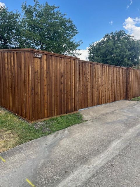 Wooden privacy fence along a driveway under a partly cloudy sky