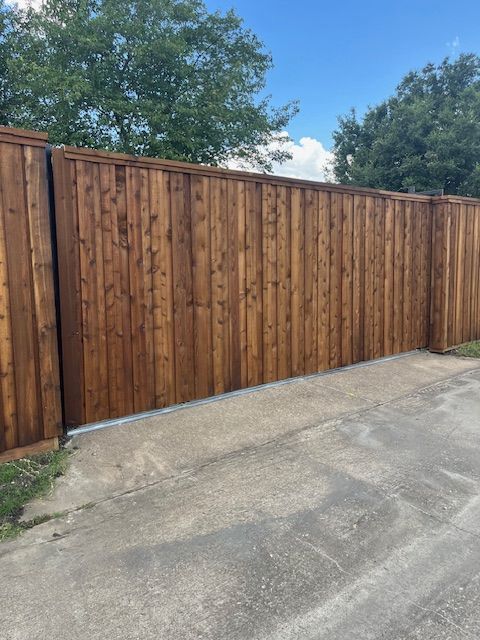 Wooden privacy fence along a concrete driveway under a partly cloudy sky