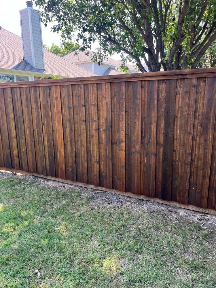 Wooden privacy fence along a grassy backyard with a tree and neighboring house roofs behind it
