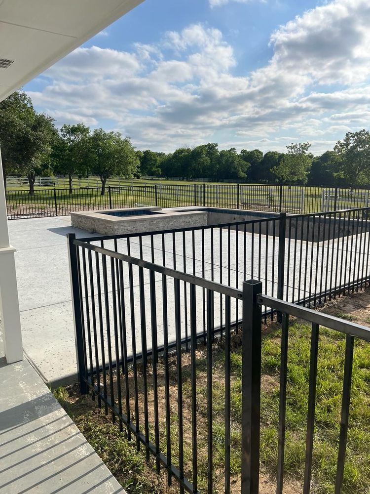 Black metal fence around a backyard patio and pool area, with trees and a cloudy sky beyond.