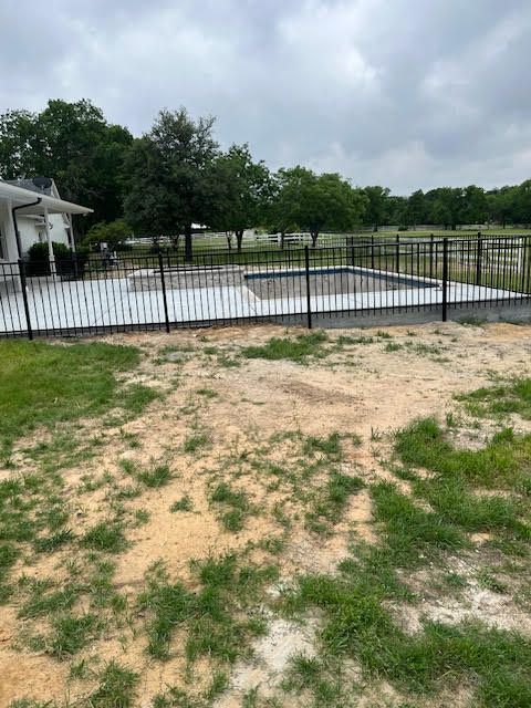 Backyard with a fenced swimming pool, concrete patio, and patchy grass in the foreground