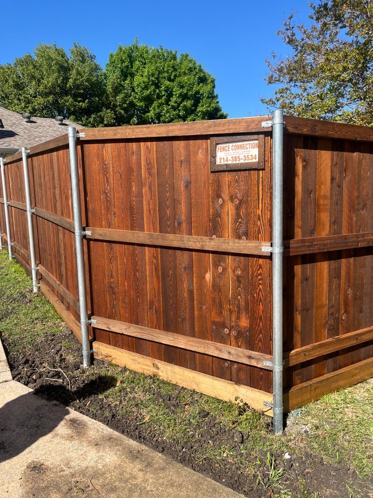 Wooden privacy fence with metal posts beside a concrete path in a sunny yard