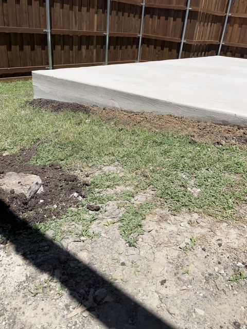 Concrete slab beside a patchy dirt yard with a wooden fence in the background.