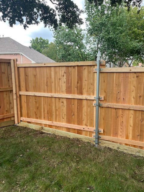 Wooden backyard fence with metal support post beside a grassy lawn and house roofline