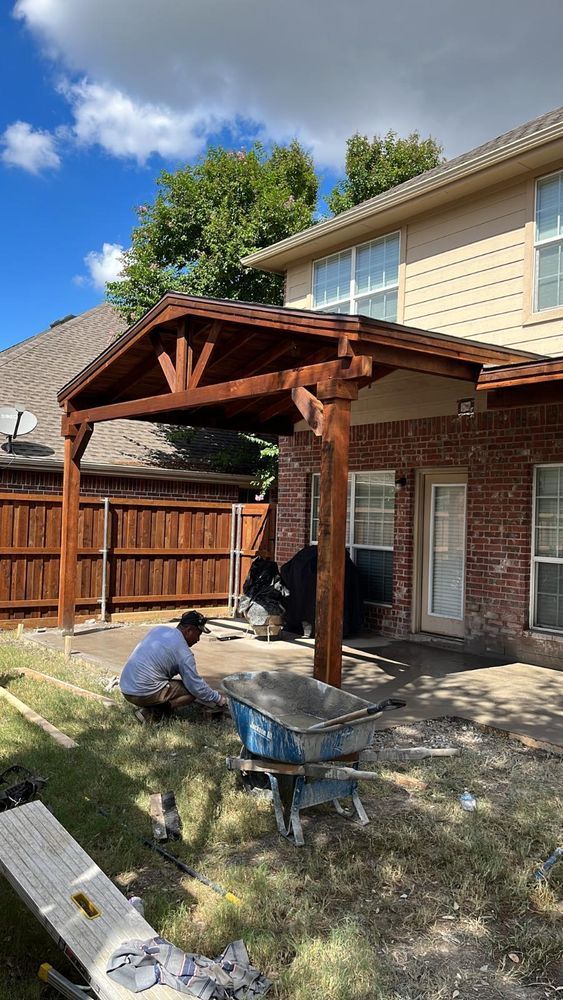 Two workers installing a wooden patio roof beside a brick house and fence