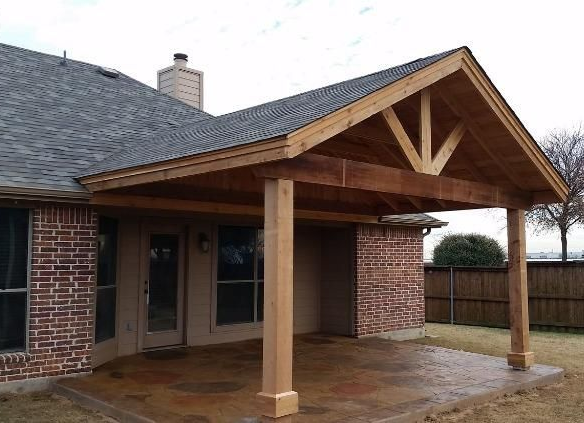 Covered patio with wooden posts and brick chimney attached to a house
