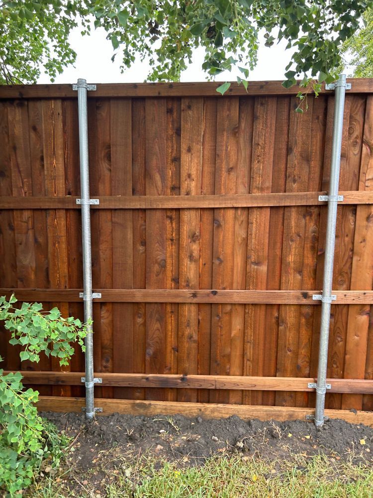 Wooden backyard fence with metal support posts and green foliage at the edges