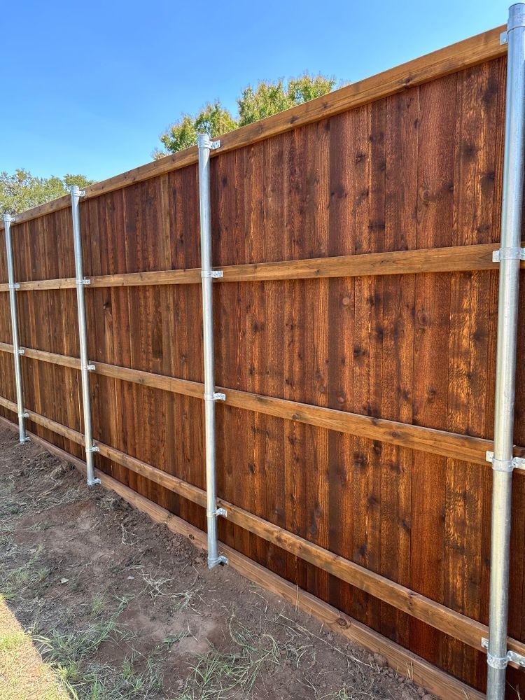 New wooden fence with metal posts along a dirt yard under a blue sky