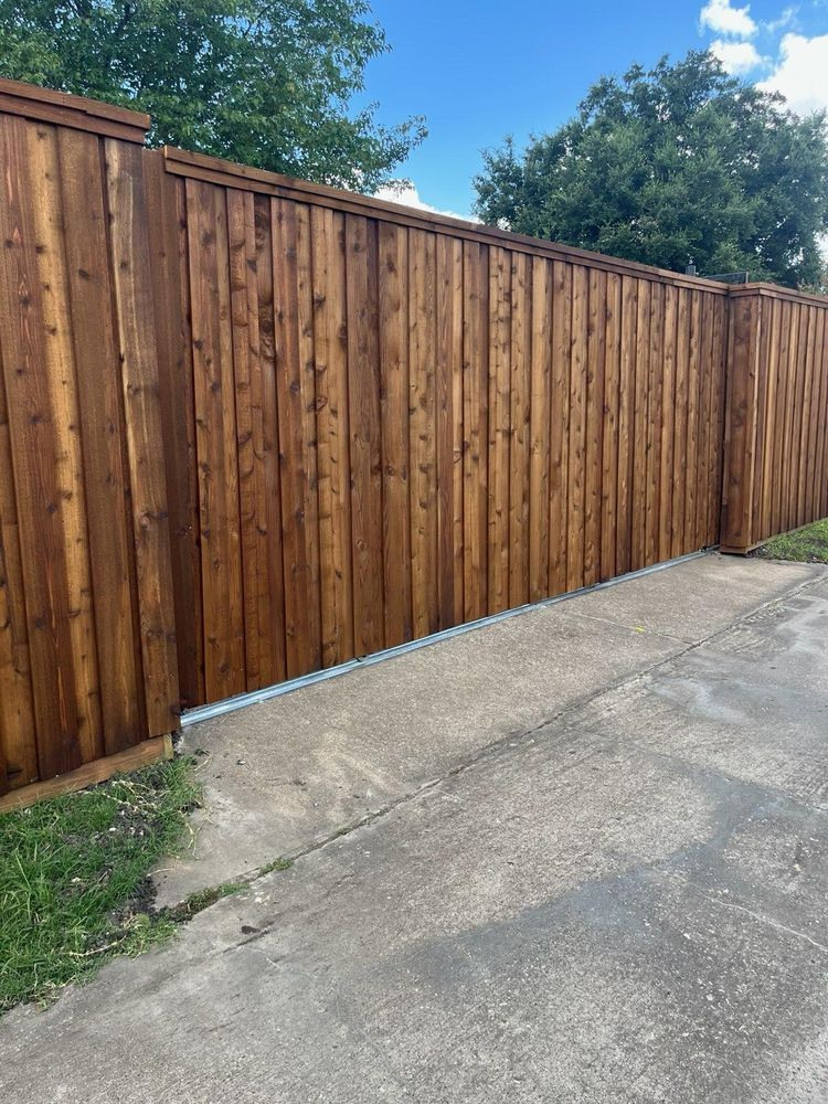Wooden privacy fence along a cracked concrete driveway with trees in the background