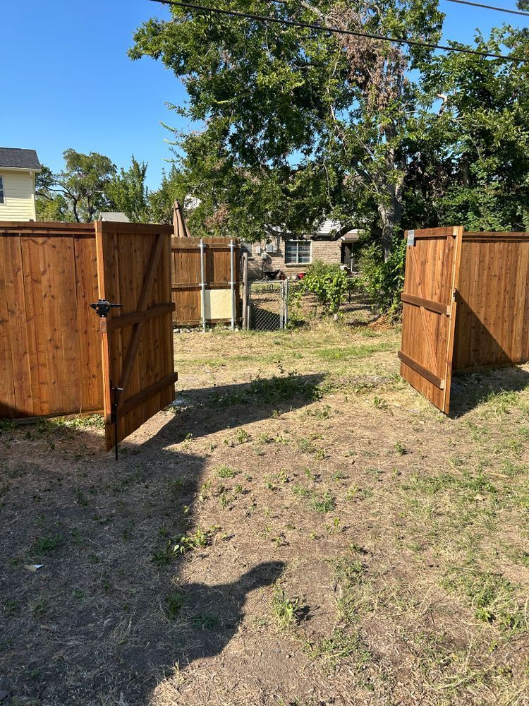 Open wooden gates leading to a backyard with a tree and grass under a bright blue sky
