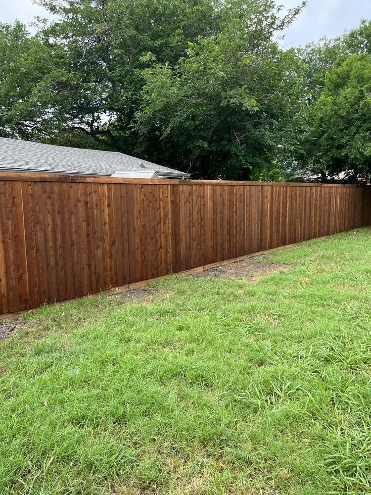 Wooden privacy fence beside a grassy yard, with trees and a house roof in the background.