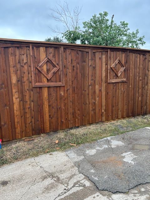 Wooden privacy fence with decorative diamond accents beside cracked pavement under a blue sky