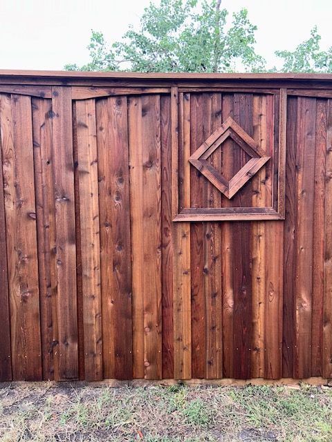 Wooden fence with a decorative diamond design panel against a grassy yard and trees.