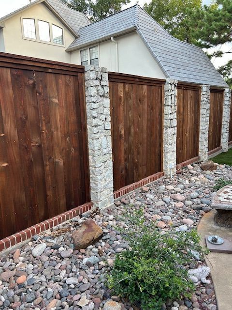 Wooden privacy fence with stone columns lining a landscaped rock garden beside a house