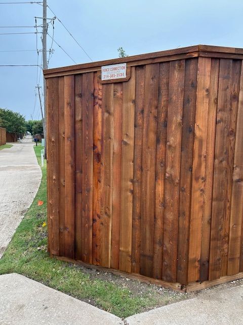 Wooden privacy fence corner beside a sidewalk and grassy strip under a clear sky