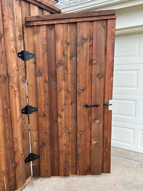 Rustic wooden gate with black hinges, partially open beside a white garage door.