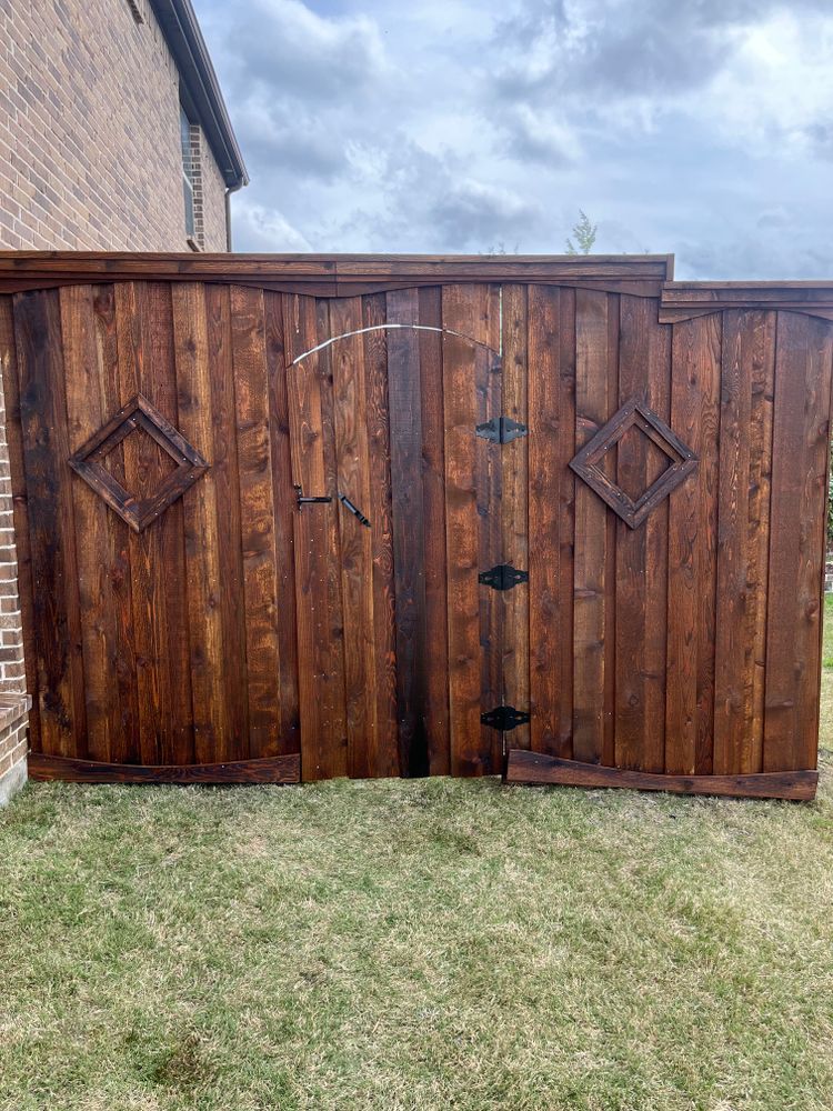 Wooden double gate with diamond accents and metal latches beside a brick house and grass yard