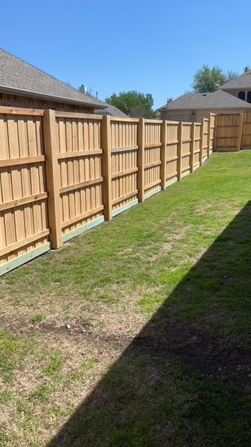 Wooden privacy fence beside a narrow grassy backyard under a sunny blue sky