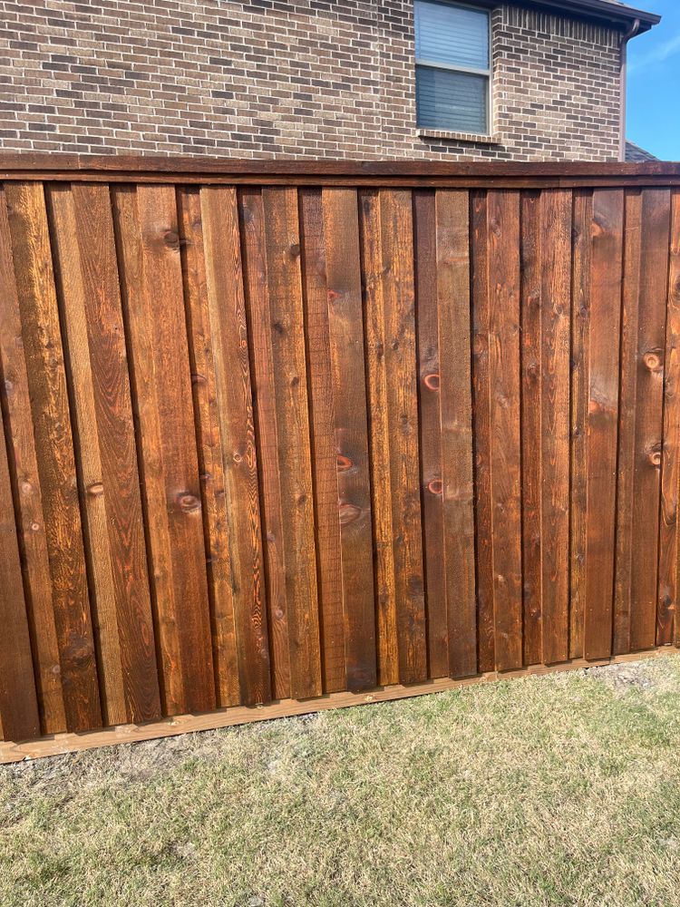 Weathered wooden fence with vertical brown planks in a yard, brick house visible above it.