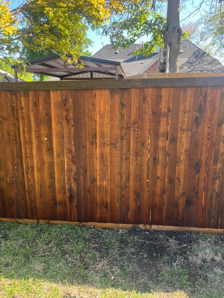 Wooden privacy fence with autumn trees and a house visible above it, beside a grassy yard.