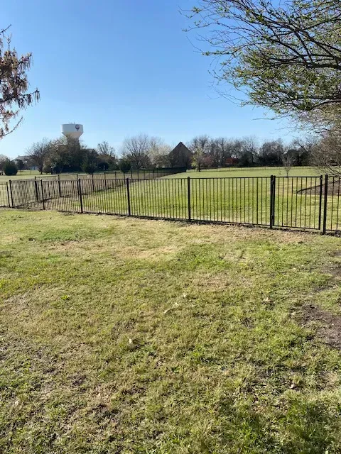 Grassy park with a metal fence, leafless trees, and a water tower under a clear blue sky