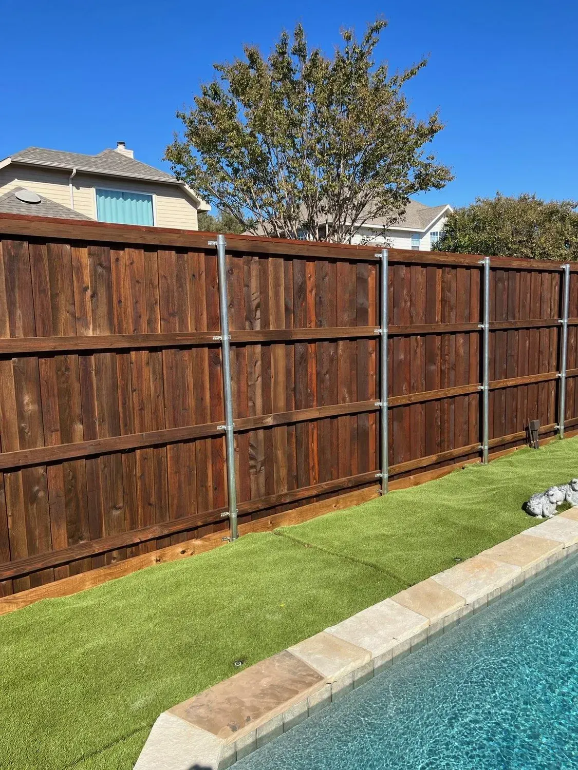 Wooden backyard fence beside a swimming pool and green lawn under a clear sky