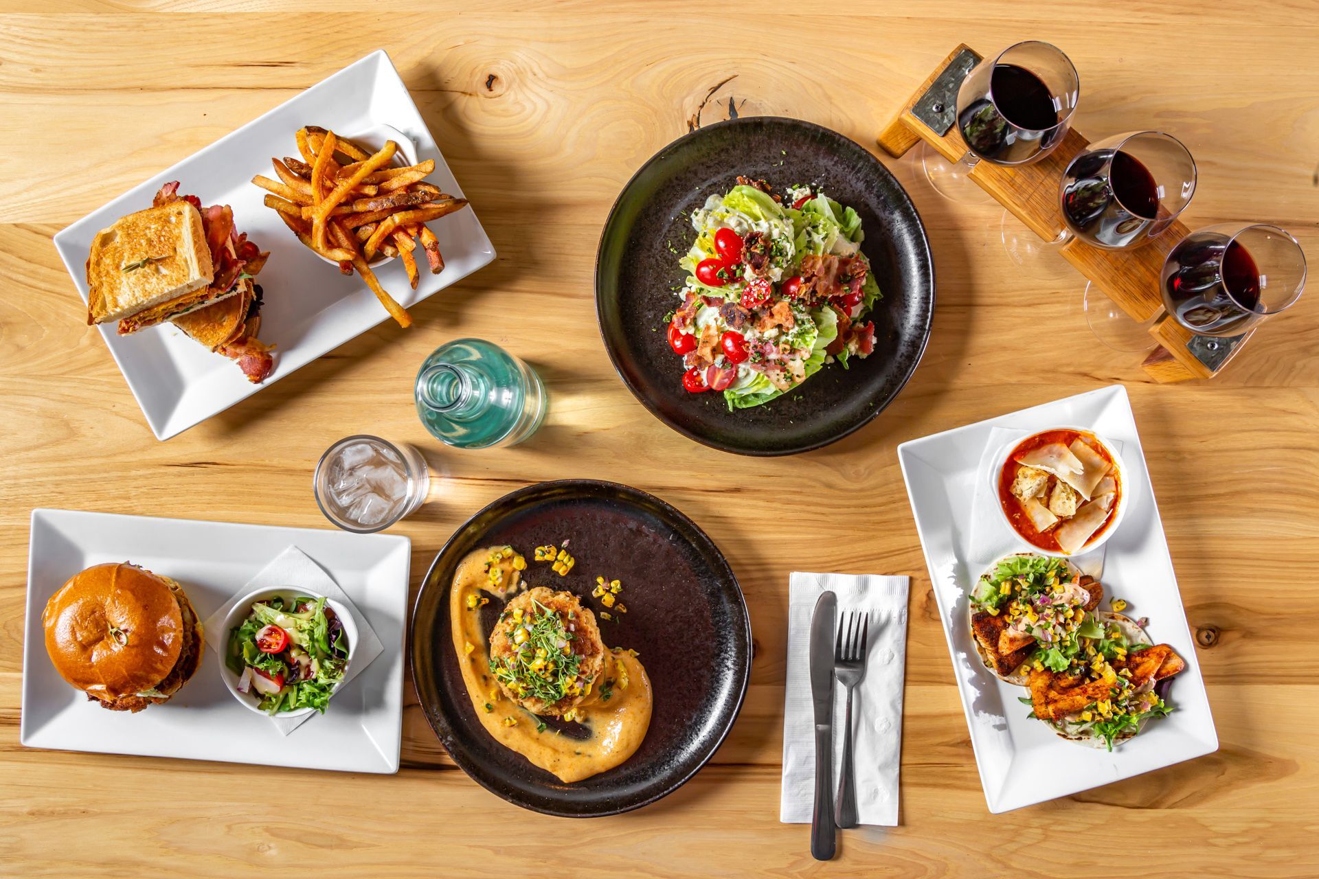 Overhead shot of a wooden table with various dishes like sandwiches, salads, and wine glasses.