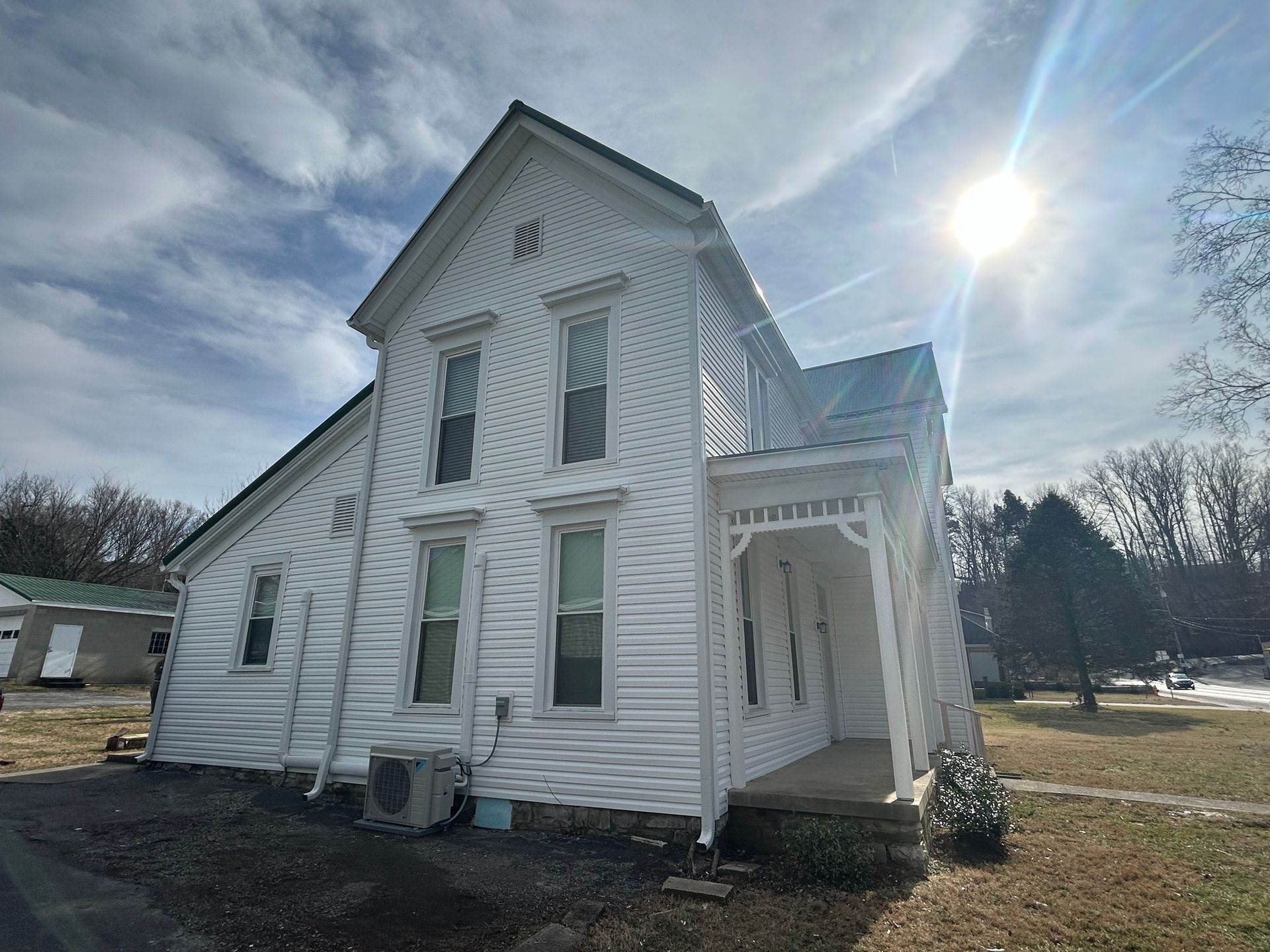 A white house with a porch and a lot of windows on a sunny day.