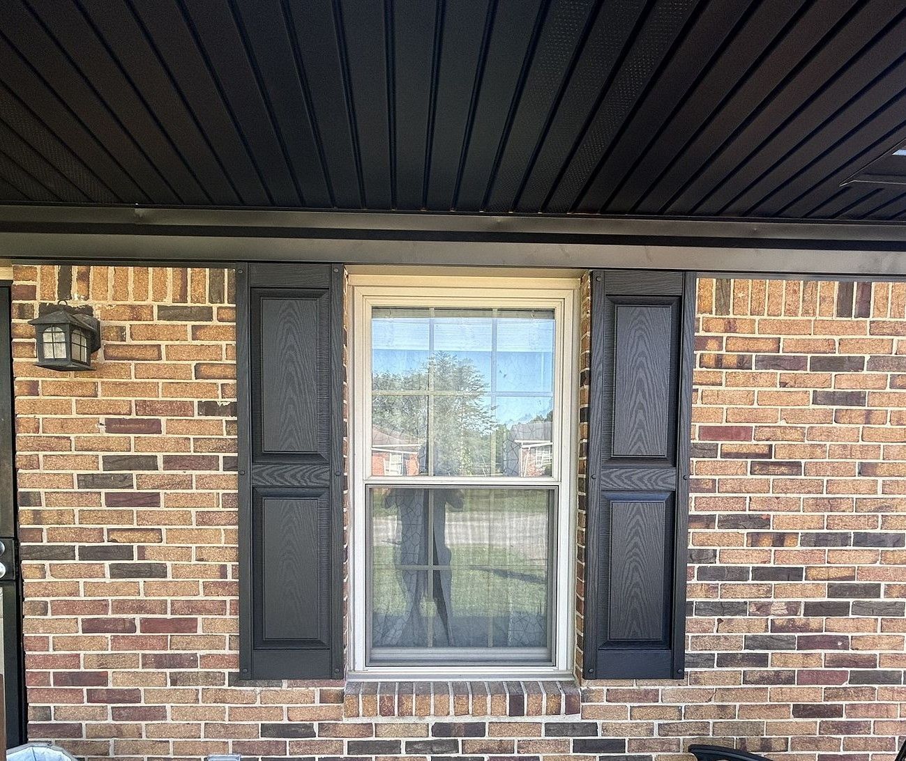 A brick house with black shutters and a window.