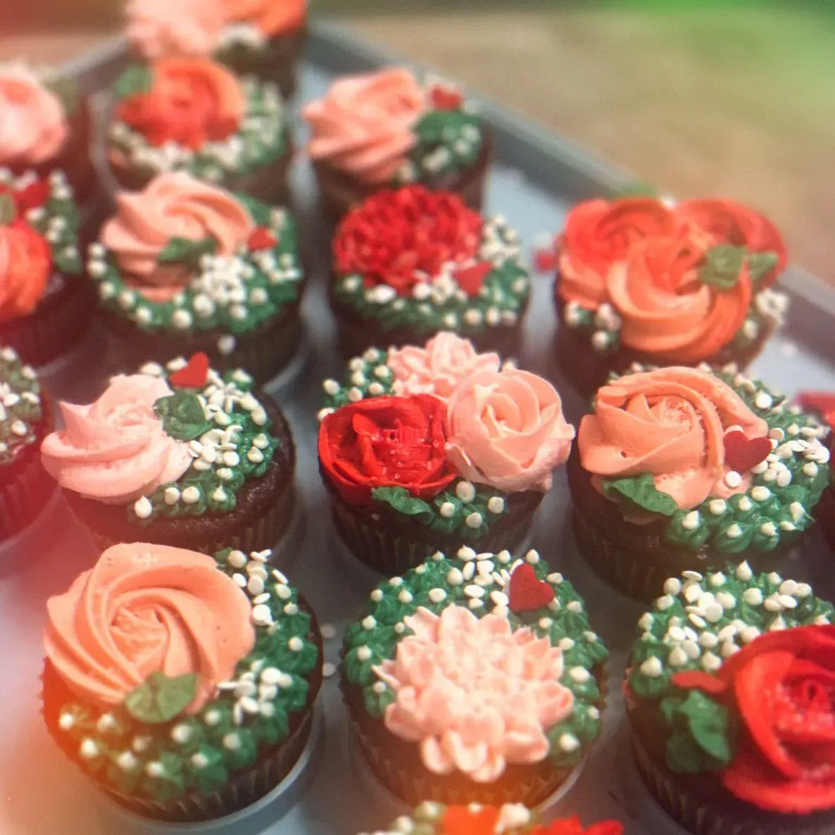 Assorted cupcakes topped with pink, red, and white frosting flowers on a tray