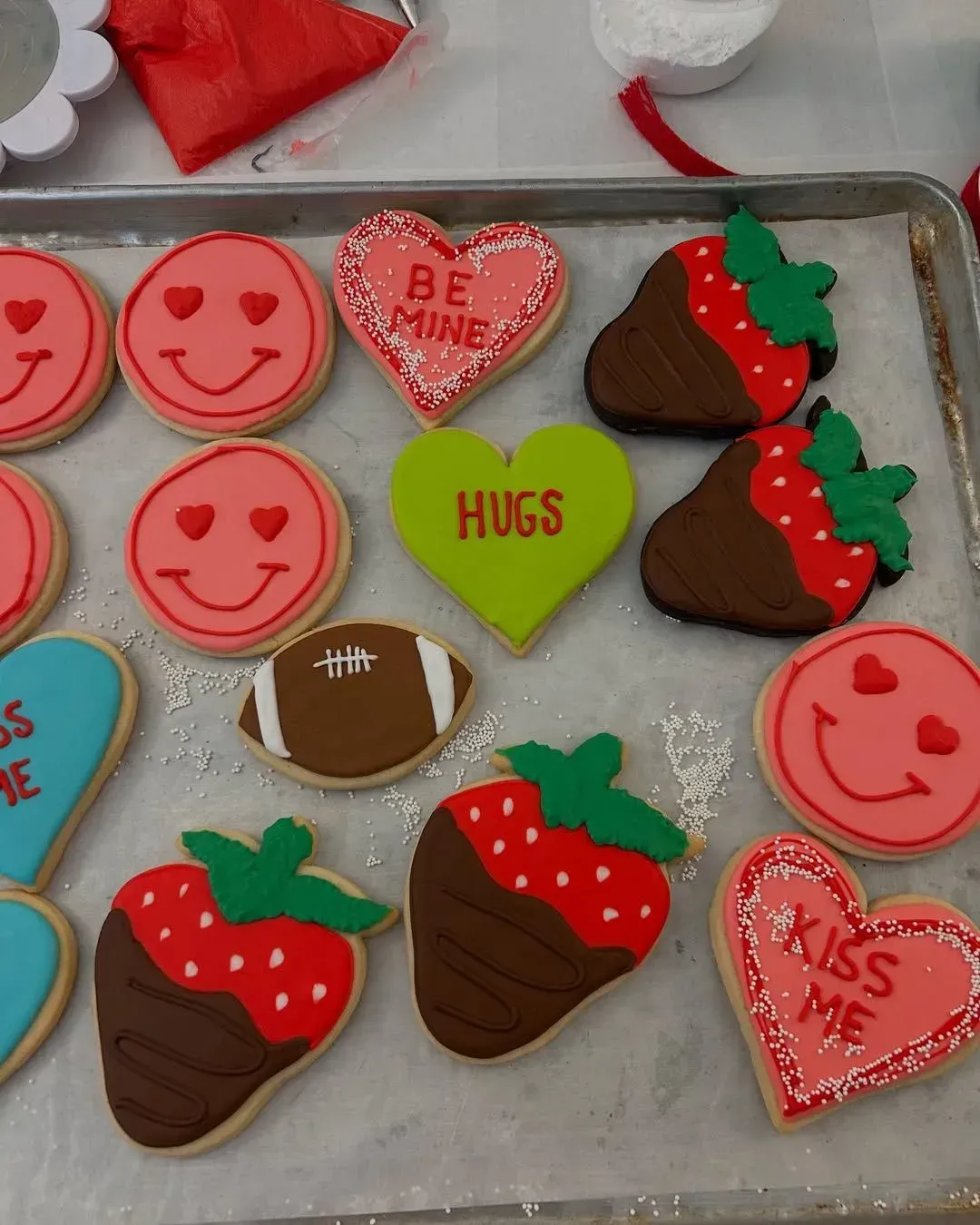 Assorted Valentine’s Day cookies with hearts, strawberries, lips, footballs, and “HUGS” and “KISS ME” designs