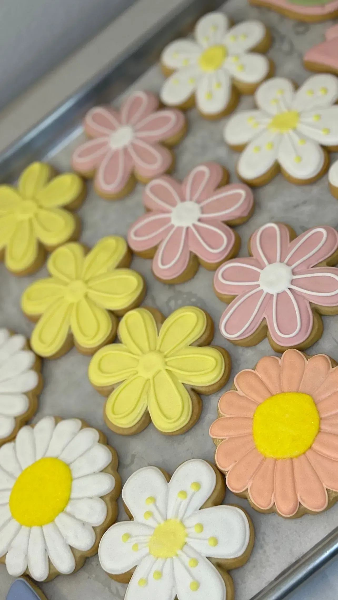 Colorful flower-shaped cookies with pastel frosting arranged on a baking tray